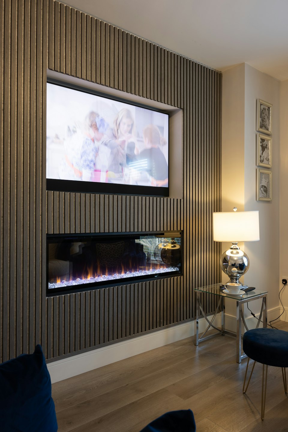 Sala de estar con pared de lamas de madera, televisión y chimenea eléctrica.